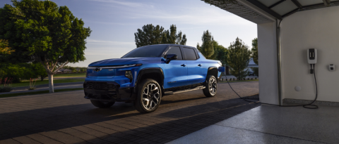 Blue Chevrolet Silverado EV charging in a driveway.