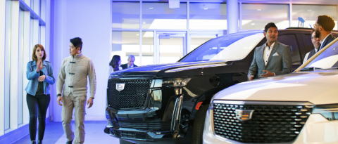 El vendedor y el cliente pasan por delante de un Cadillac Escalade en un concesionario con iluminación púrpura.