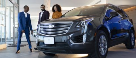 Couple discussing their first auto loan with a salesman at a Cadillac dealership.