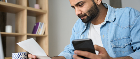 Un hombre de negocios joven con un teléfono leyendo un recibo bancario y calculando los impuestos