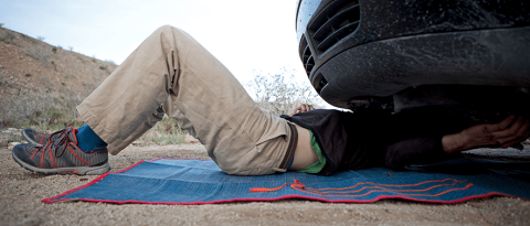 hombre debajo de un vehículo en una carretera haciendo reparaciones