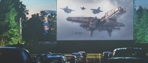 Cars facing a drive-in movie screen at sunset