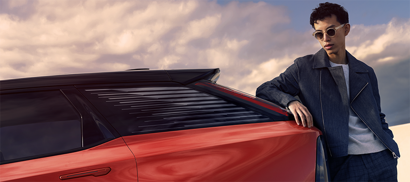 A man with shades leans against a red vehicle