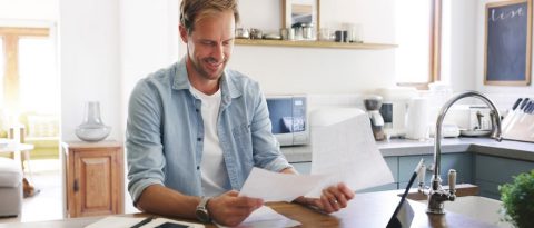 Smiling man reviewing interest loans in his kitchen