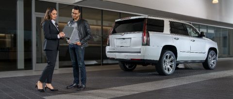 two people looking at a tablet in front of a cadillac