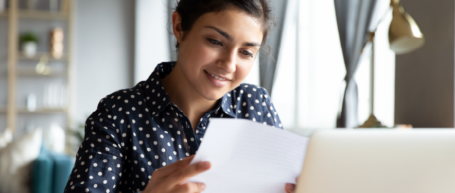 Woman sitting in front of her computer while reviewing a paper document.