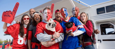 A crowd of sports fans and two dogs celebrating and tailgating