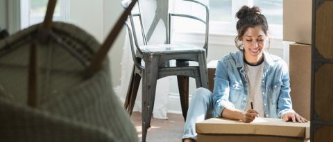 Woman writing a label on a box while moving out for the first time