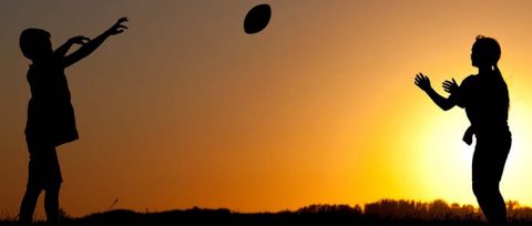 Silhouette of two children tossing a football at sunset