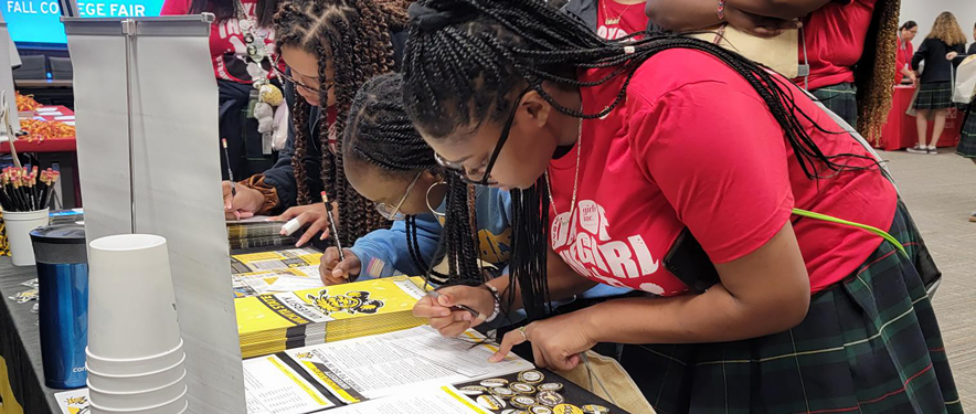Three women signing forms at Fall College Fair