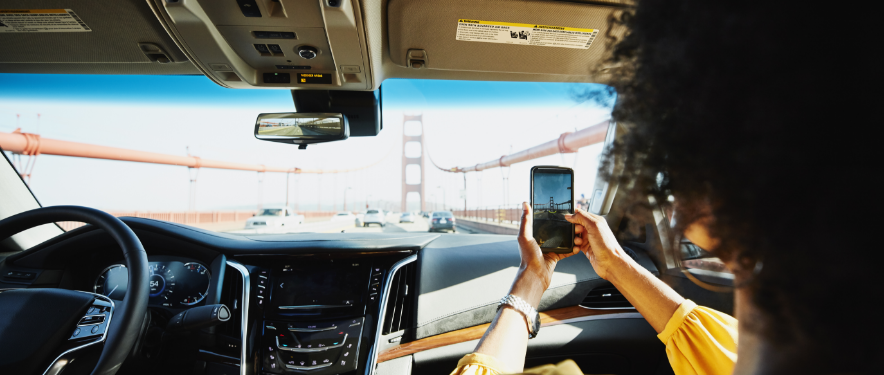 Woman photographs Golden Gate Bridge from car passenger seat