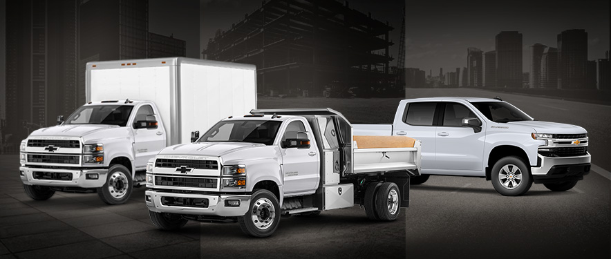 Three types of commercial trucks, all white in front of a dark cityscape background. 