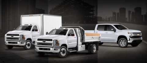 Three types of commercial trucks, all white in front of a dark cityscape background.