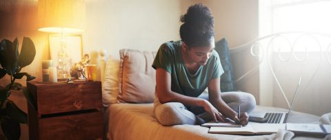 College student doing work on her dorm room bed.