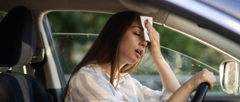 Woman in car with window down, wiping her forehead