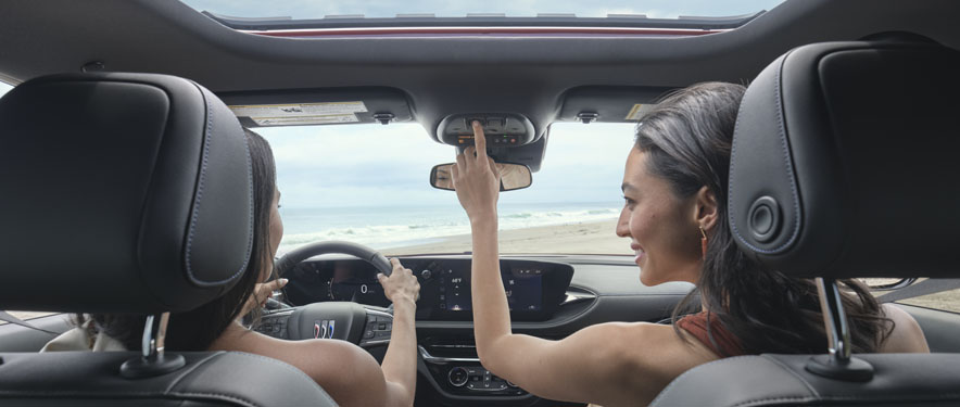 Back seat view of two women in a Buick at the beach.