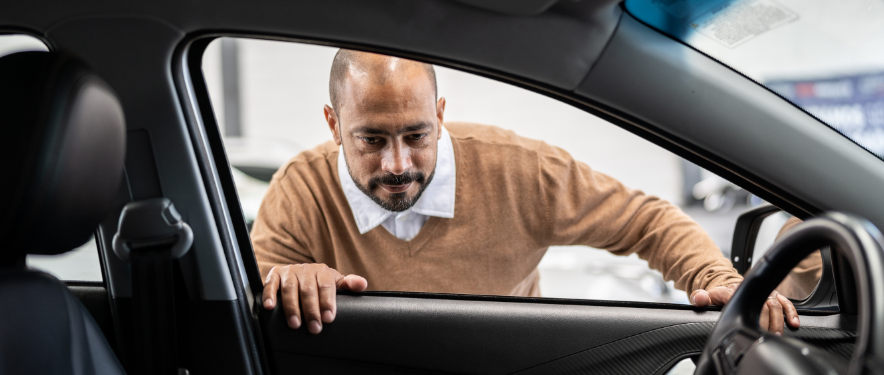 Un hombre calvo inspecciona el interior de un vehículo de GM mientras reflexiona sobre el costo real de ser propietario de un vehículo.