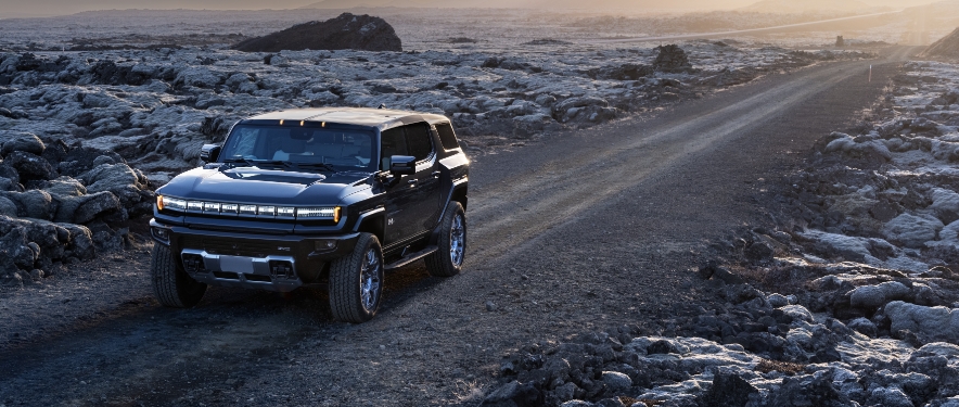 GMC HUMMER EV driving on a dirt road at sunset.