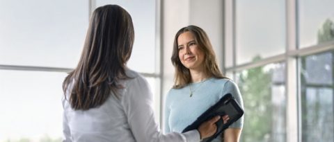 Woman listening while a GM salesperson tells her about the GM Rewards program using a tablet.