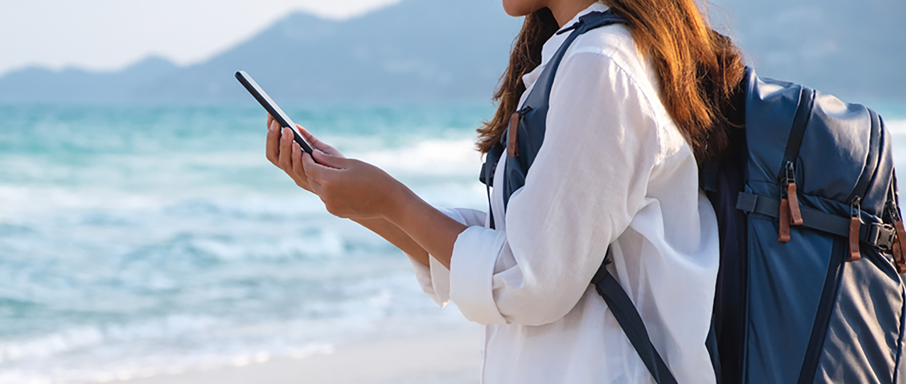 Backpacker checking her MyAccount on the GM Financial Mobile app while standing on a beach.