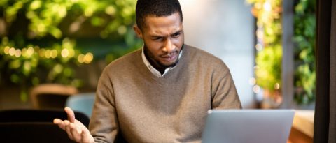 A cautious person at their laptop, looking skeptical while reading an email.