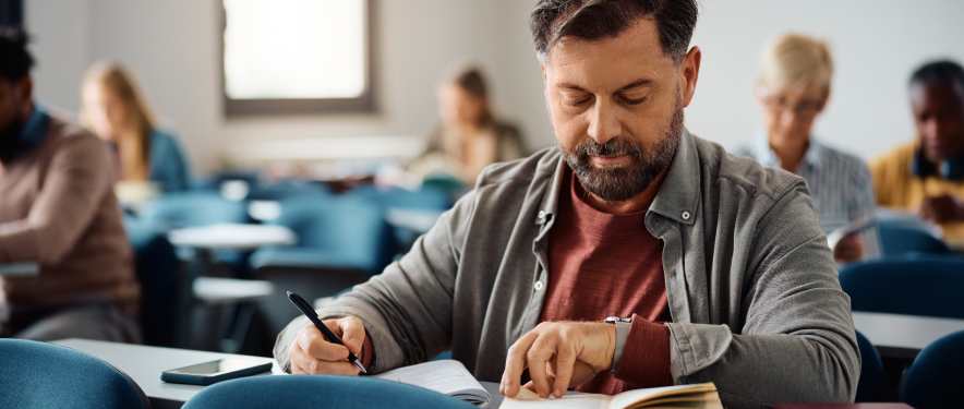 Middle-aged man taking notes in a college classroom.