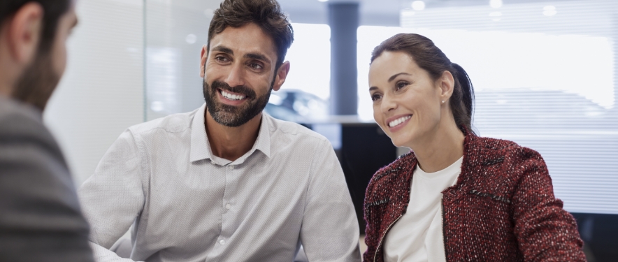 A couple reviews their long-term auto financing with a dealer in an office.