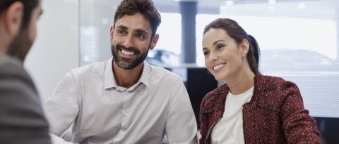 A couple reviews their long-term auto financing with a dealer in an office.