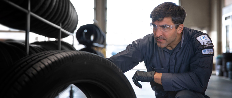GM Certified Service technician inspecting tires in a garage.