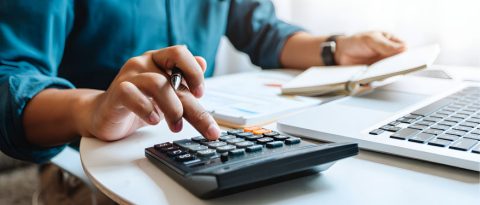 Person in a teal dress shirt reviewing their monthly budget with a calculator.