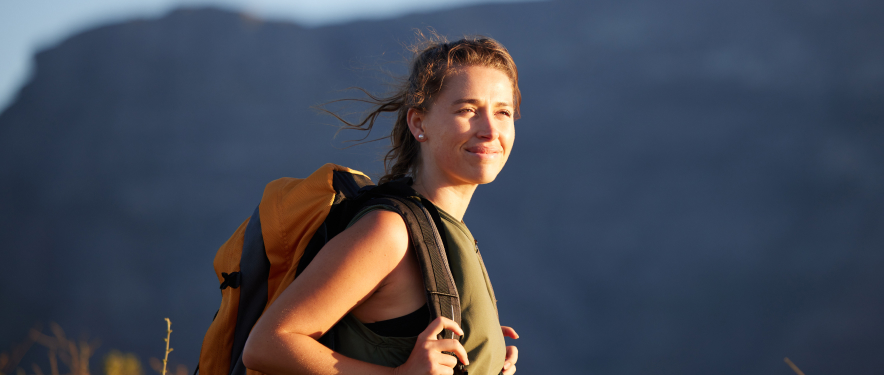 Smiling woman with backpack on a hiking trip she paid for by investing.